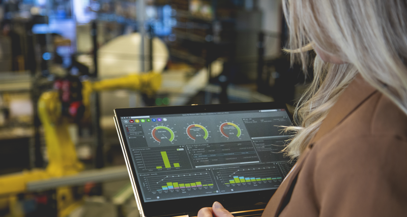 A person holding a tablet computer in a factory environment displaying Monitor ERP dashboard. 