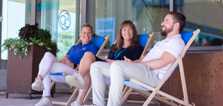 Tre anställda på Monitor sitter i solstolar och pratar utanför huvudkontoret i Hudiksvall.