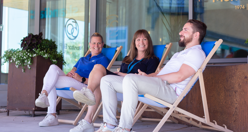 Tre anställda på Monitor sitter i solstolar och pratar utanför huvudkontoret i Hudiksvall.