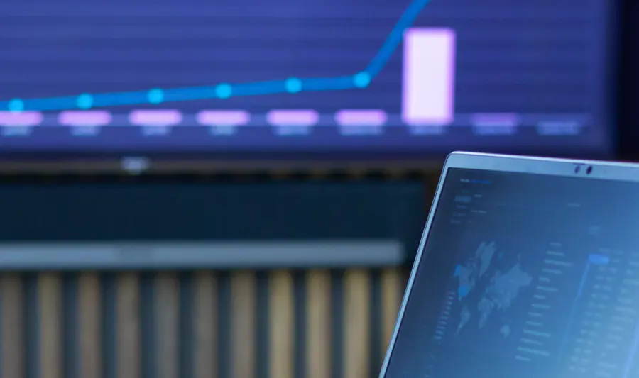 Laptop na stole z uruchomionym systemem Monitor ERP, a w tle ekran z danymi z Monitor BI.