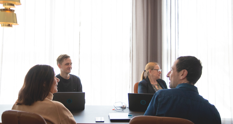 A group of people sitting around a table with laptops.