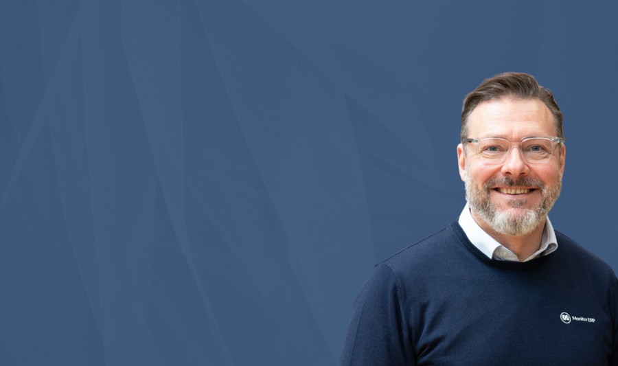 Juha Kalliola, myyntipäällikkö Monitor ERP:llä, seisoo sinisen taustan edessä.