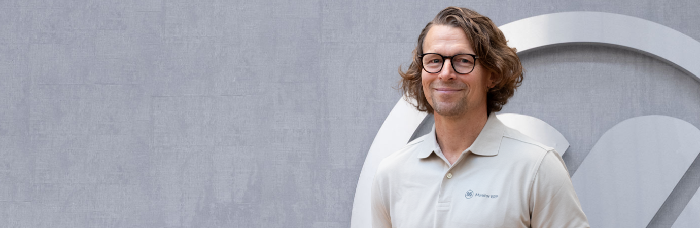 A man with glasses standing in front of a wall.