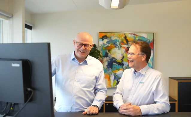 Two men standing in front of a computer looking at Monitor ERP looking happy.