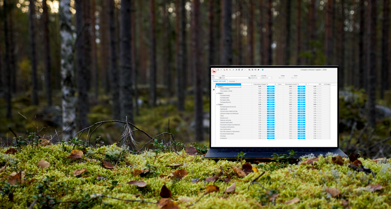 A laptop computer displaying Monitor ERP and its sustainability functionality sitting on top of a moss covered ground surrounded by trees.