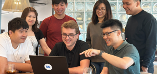 A group of people sitting around a table with a laptop.