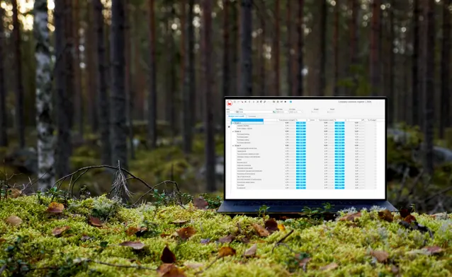 A laptop computer displaying Monitor ERP and its sustainability functionality sitting on top of a moss covered ground surrounded by trees.