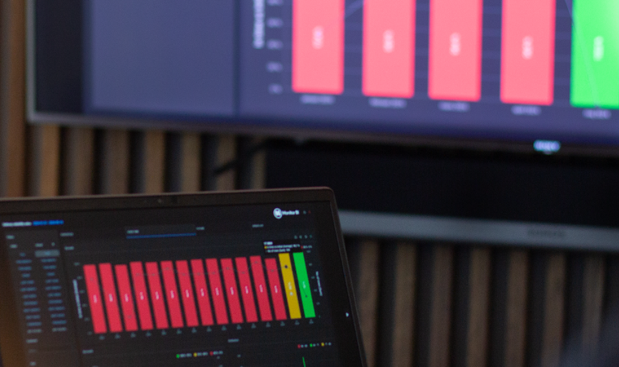 laptop on a table and a screen on a wall, showing Monitor ERP Dashboard