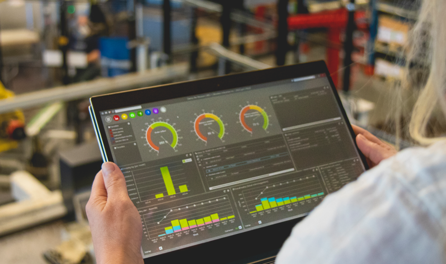 Kobieta na hali produkcyjnej, trzymająca tablet z pulpitem nawigacyjnym systemu Monitor ERP