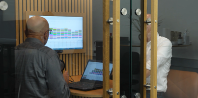 A man standing in front of a laptop computer displaying Monitor ERP dashboards. 