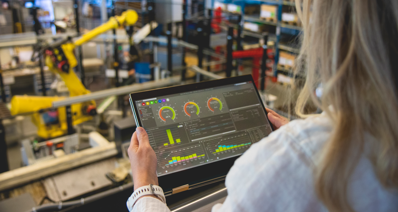 A person holding a tablet computer in a factory environment displaying Monitor ERP dashboard. 