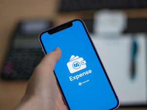 A person holding a cell phone with a Monitor Expense logo.